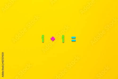 Mathematical example one plus 1 is equal on yellow background made of children plastic numbers. The first steps in mastering maths in elementary school. Simple action. Educational game. Task solution photo