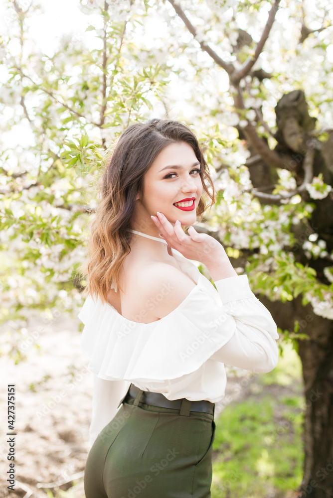 Lovely young girl in a white romantic silk blouse in spring in a blooming cherry garden in sunny weather. Spring and Fashion. Spring blooming gardens Lovely young girl in a white romantic silk blouse in spring in a blooming cherry garden in sunny weather. Spring and Fashion. Spring blooming gardens