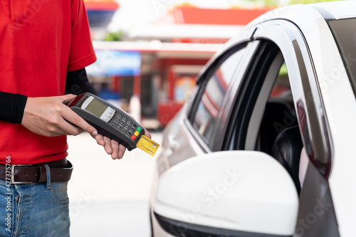 Service worker holding credit card reader for payment at gas station. Refuelling car and service payment with wireless bank payment terminal at gas pump