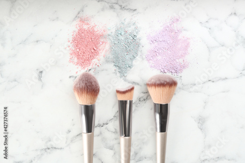 Makeup brushes and scattered eye shadows on white marble table, flat lay