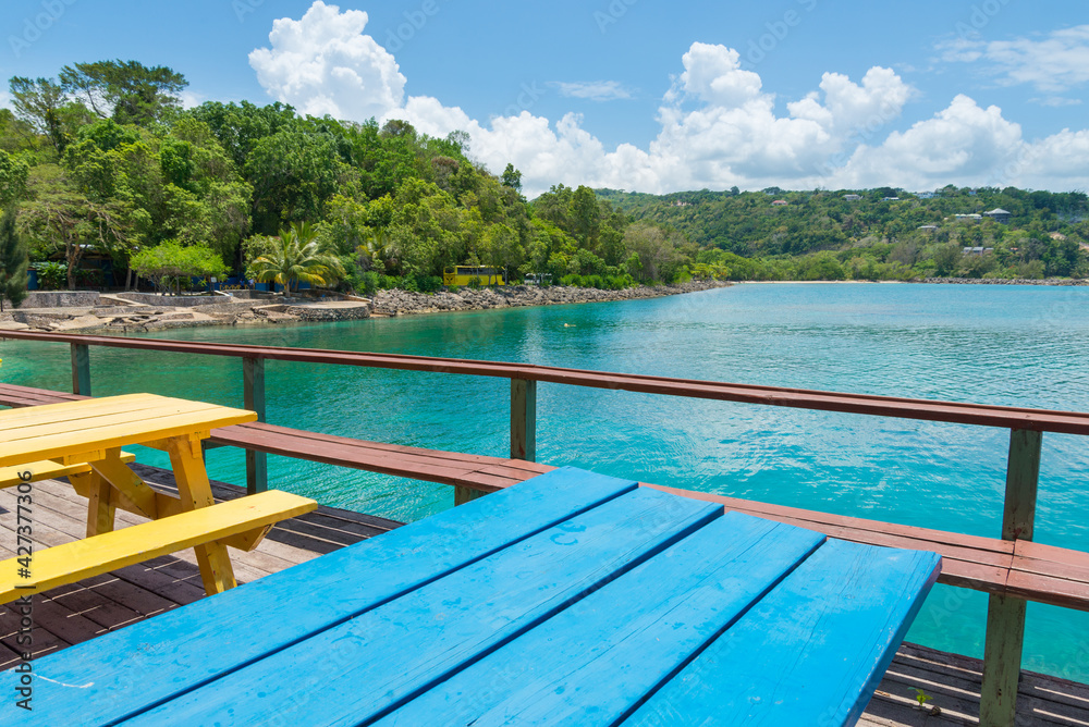 James Bond Beach, Jamaica. A view of the bay, with turquoise waters and green trees in the background. Colorful tables in the foreground.