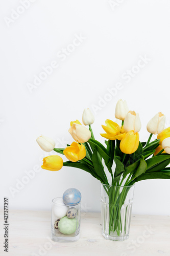 Easter eggs in a glass and yellow tulips in a vase on a light background