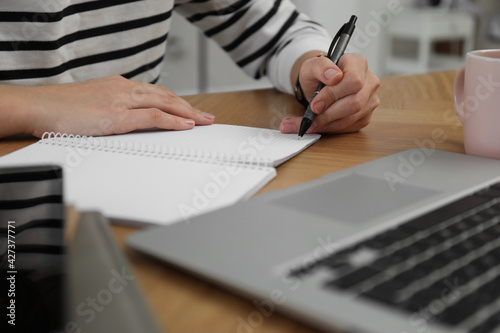 Left-handed woman writing in notebook at wooden table indoors, closeup