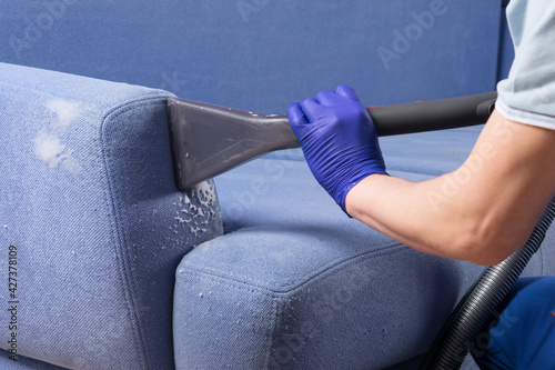 close-up of a hand in a protective glove, cleaning the blue sofa from dirt © kurgu128