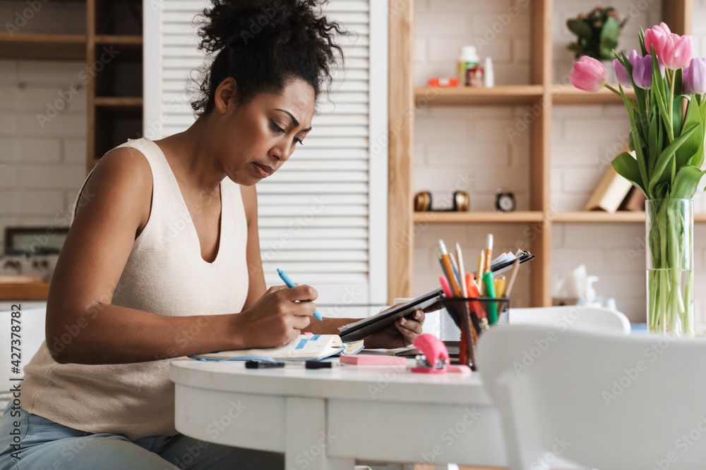 Black woman working with laptop and papers while sitting at table Black woman working with laptop and papers while sitting at table