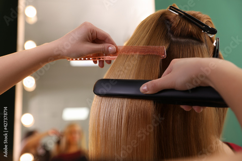 Konstfotografi Stylist straightening woman's hair with flat iron in salon
