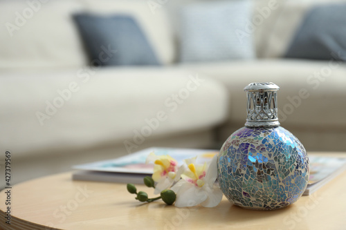 Stylish catalytic lamp with orchid on wooden table in living room, space for text. Cozy interior photo