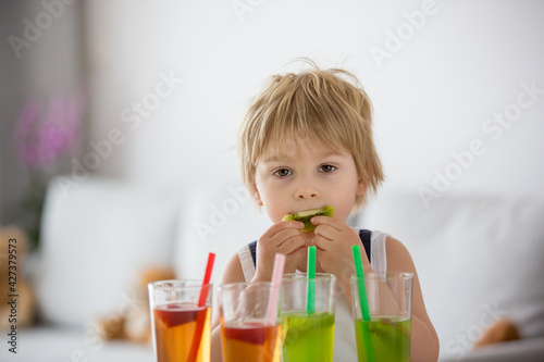 Cute toddler child, blond boy, drinking freshly made fruit juice at home