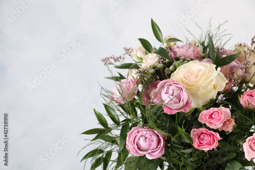 Beautiful bouquet with roses on light blue background, closeup. Space for text