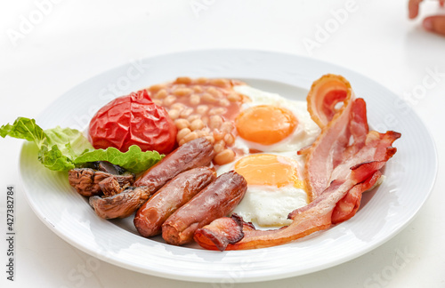 traditional English breakfast with sunny side up egg toast tomatoes bacon sausage and baked beans.