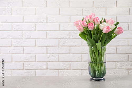 Beautiful bouquet of tulips in glass vase on light table. Space for text