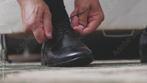 The man is tying the shnzrki on black shoes. Putting on men s shoes in the morning before going to work. Hands close-up
