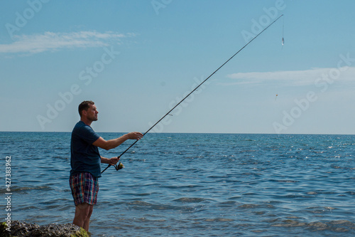 man with fishing rod. stands on the ankle in sea water on the stones