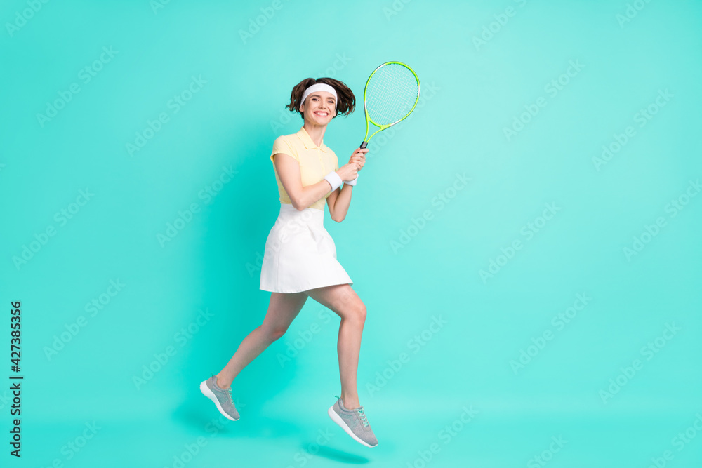 Full size photo of happy cheerful good mood girl jumping playing tennis exercising isolated on turquoise color background Full size photo of happy cheerful good mood girl jumping playing tennis exercising isolated on turquoise color background