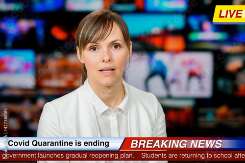 An anchorwoman reporting live breaking news sitting in Tv studio. Background of multiple screens of broadcast control room. Journalism concept photo