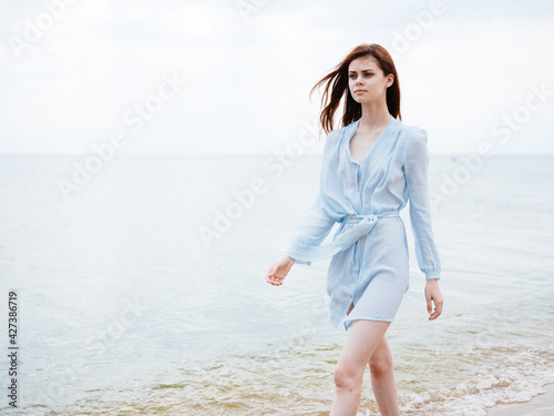 A traveler in a blue dress runs along the seashore on the beach