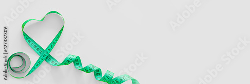 Green plastic measure tape with metric scale in the shape of a heart over on grey background. Top view, copy space