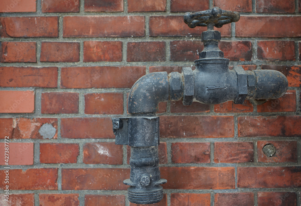 Dirty water faucets and pipes on the wall of an old brick building