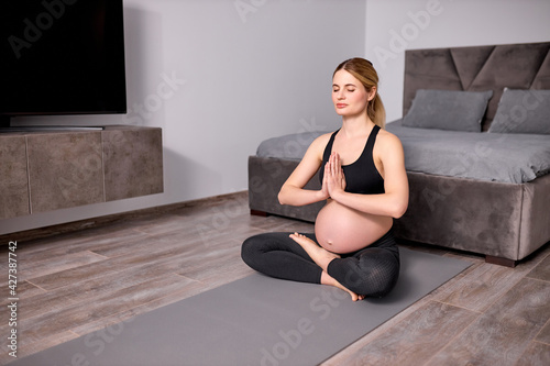 side view on calm pregnant female sitting on floor, keeping hands together, namaste