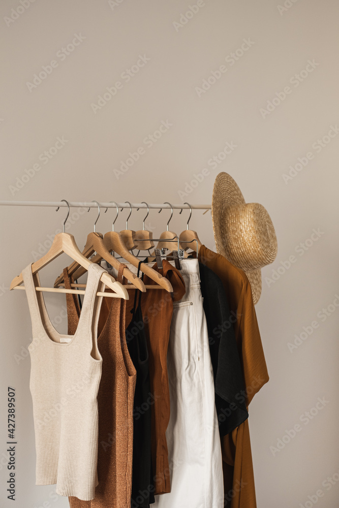 Foto Stock Aesthetic minimalist fashion influencer blog composition.  Stylish pastel summer female clothes, dress, tops, t-shirts, straw hat on  clothing rack against white wall. Fashion women wear | Adobe Stock