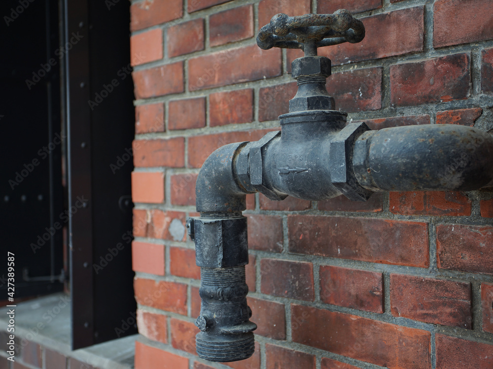 Dirty water faucets and pipes on the wall of an old brick building