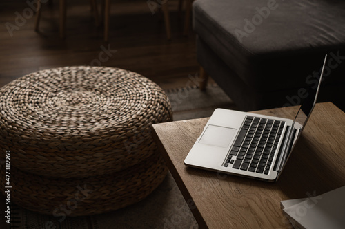 Modern interior design. Stylish bright living room decorated with solid wood table, rattan pouf, laptop computer. Aesthetic minimalist living room.