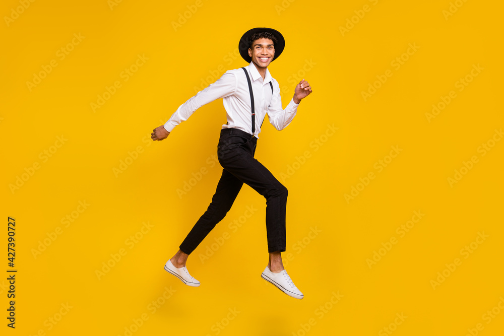 Photo of energetic sporty guy jump run wear headwear shirt suspenders footwear isolated yellow color background