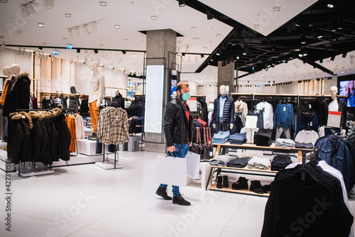 An urban young handsome man with a mask and bags in his hand walks in a boutique. Shopping in the mall during the pandemic COVID - 19 coronavirus