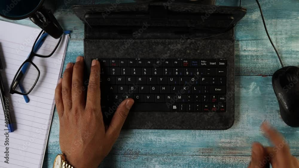 Top view of hands of an Indian man typing in keyboard of mini computer on wooden table