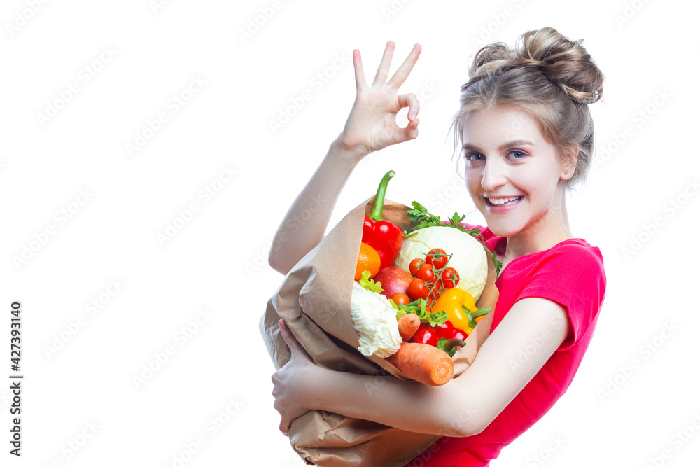 Young Caucasian Female Holding Eco Paper Bag Filled With Multiple Vegetables and Groceries Posing With OK Gesture Against White Background. Young Caucasian Female Holding Eco Paper Bag Filled With Multiple Vegetables and Groceries Posing With OK Gesture Against White Background.