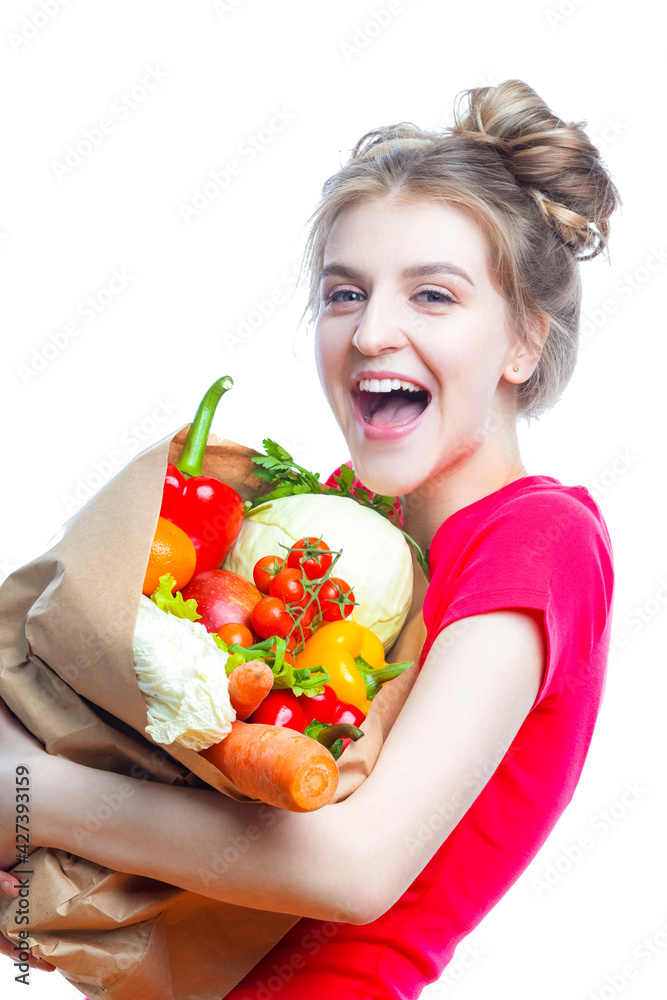 Young Caucasian Female Holding Eco Paper Bag Filled With Multiple Vegetables and Groceries Posing Against White Background. Young Caucasian Female Holding Eco Paper Bag Filled With Multiple Vegetables and Groceries Posing Against White Background.