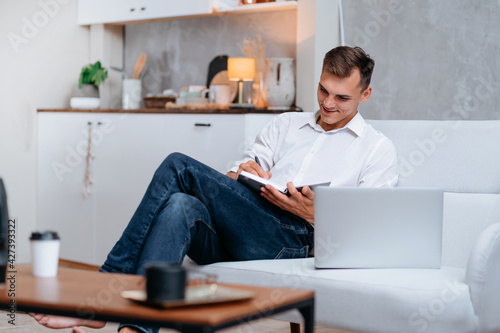 young man taking notes sitting on the couch .