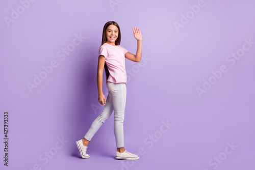 Photo of adorable pretty young girl wear pink t-shirt waving arm walking isolated violet color background