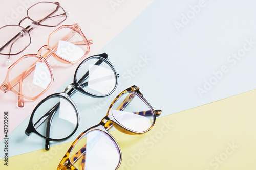 multiple eyeglasses on a multicolored background of pastel colors, geometric background, pink yellow and light blue colors, trendy eyeglass frames