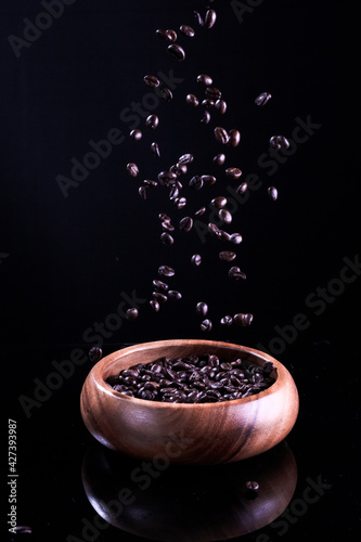 Closeup of Large Amount of Falling Fresh and Roasted Coffee Beans To Wooden Bowl Against Black Background.