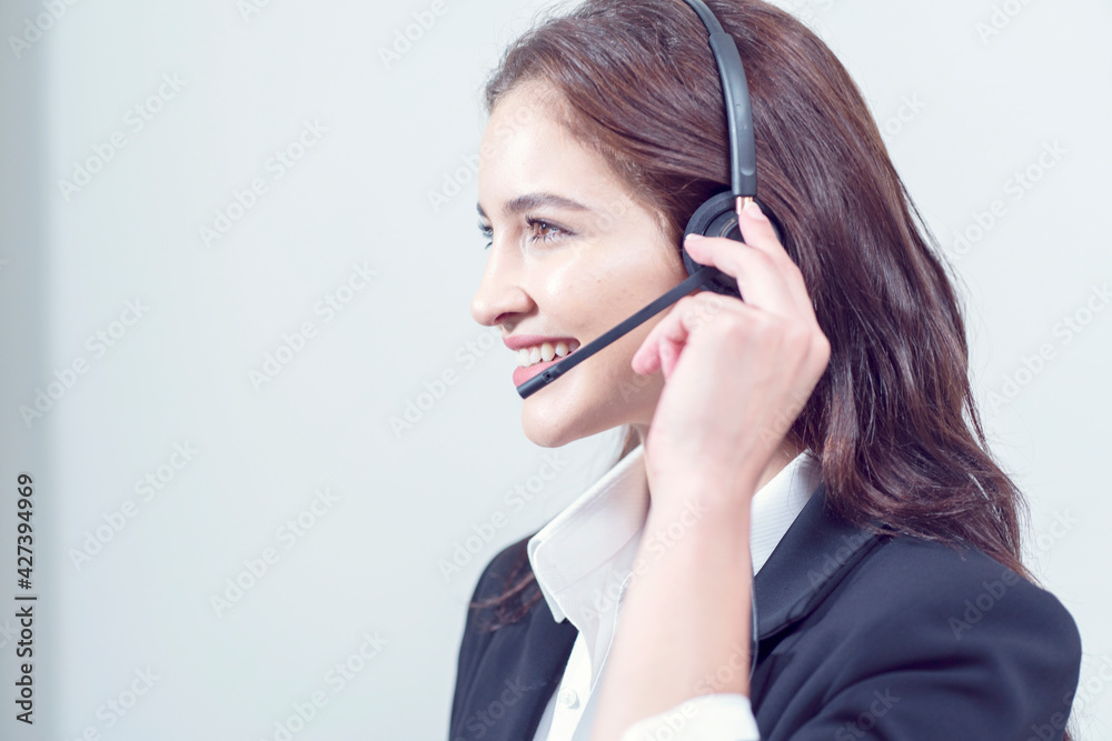 Smiling friendly female call-center agent with headset working on support hotline in the office Smiling friendly female call-center agent with headset working on support hotline in the office
