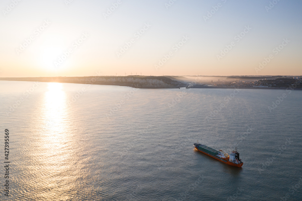 Naklejka premium Vue aérienne panoramique par drone d'un porte-conteneurs industriel arrivant à un port normand, près de la côte et des falaises de Fécamp