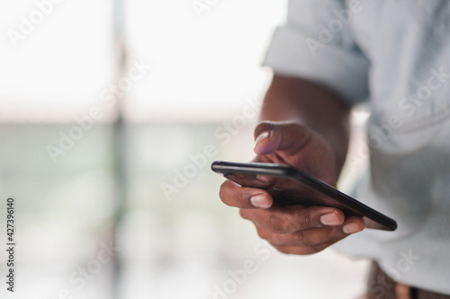 A businessman standing at the window playing a smartphone discussing a business investment project.  © Treecha