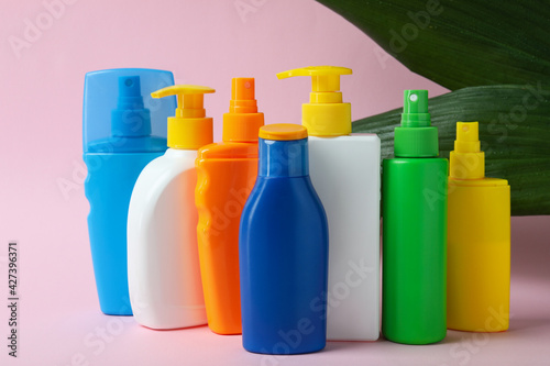 Blank bottles of sunscreens and leaves on pink background