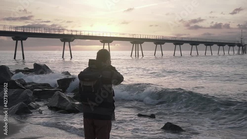 Photographer wearing backpack taking pictures of the sunrise and seascape at the beach