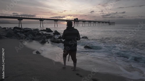 Professional Landscape Photographer Carrying a Tripod and Backpack at the beach at Sunrise