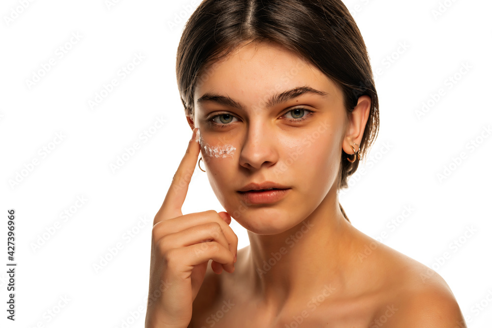 A young beautiful girl applies a skin product on her face A young beautiful girl applies a skin product on her face
