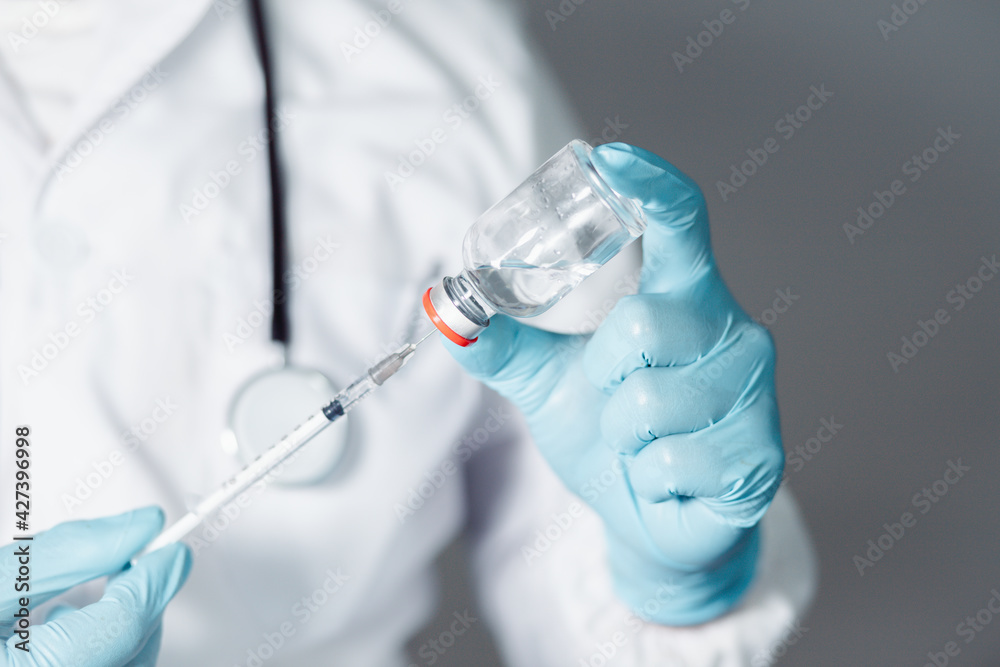 Fototapeta premium A doctor or scientist in a laboratory develops a medical vaccine. Holds a syringe with liquid vaccines to study and analyze antibody samples for new strain of COVID-19 patients in 2021. 