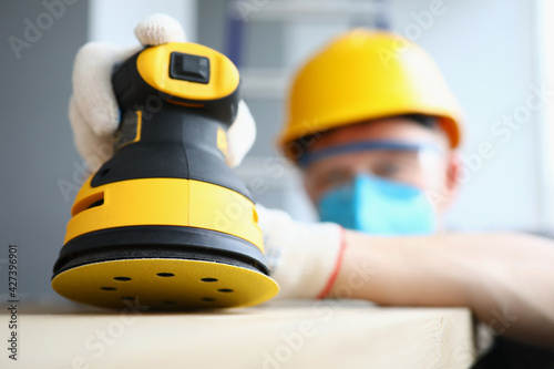 Φωτογραφία Construction foreman in helmet mask works with grinder