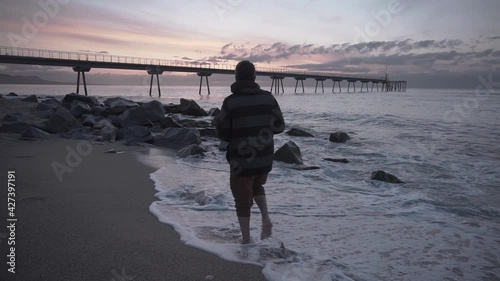 Landscape photogrpher walking barefoot on the beach and stopping to take a photo of the sea at sunrise