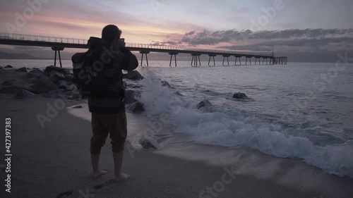Landscape photographer wearing a backpack taking photos of the sunrise at the beach