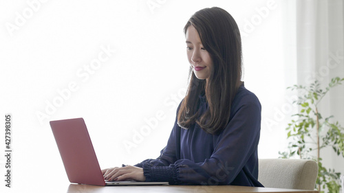 家でパソコンを使い仕事する若い女性 © polkadot