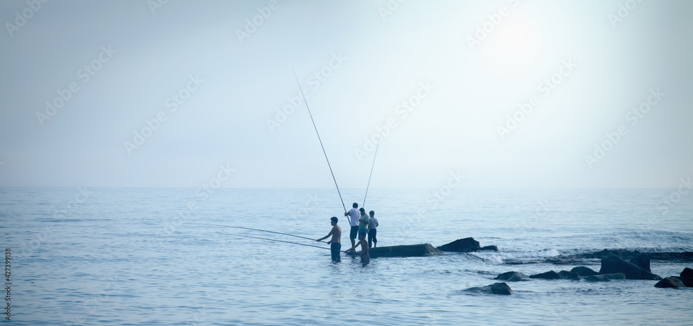Silhouette of fishermen fishing at sea outdoors with a fishing rods. Summer leisure, sport, holiday concept. Horizontal image.