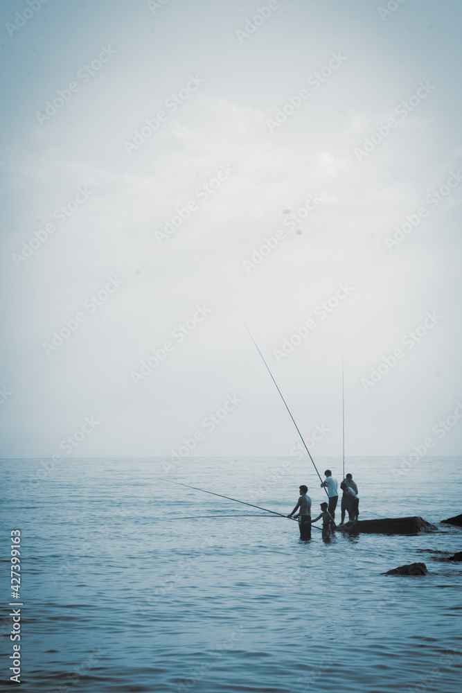 Silhouette of fishermen fishing at sea outdoors. Summer leisure, sport, holiday concept. Vertical image.
