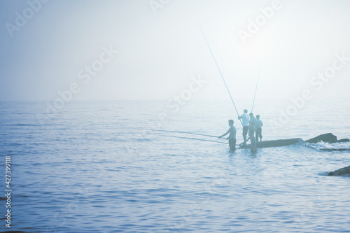 Silhouette of fishermen fishing at sea outdoors with a fishing rods. Summer leisure, sport, holiday concept. © zwiebackesser